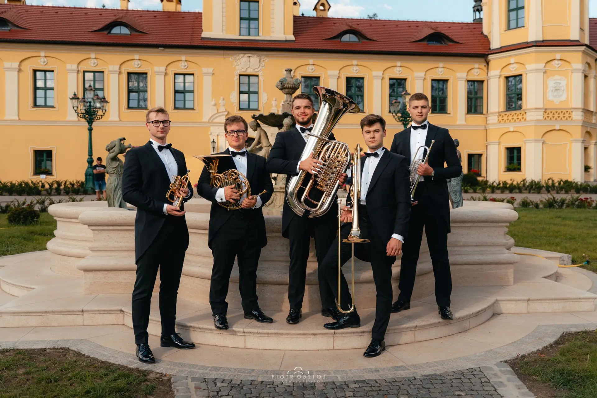 Pięciu muzyków Silver Brass z trąbkami, waltornią, puzonem i tubą przed pałacem