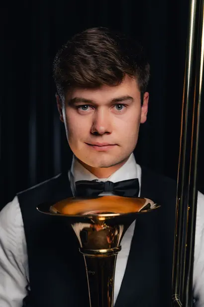 Szymon Klimański, puzonista i aranżer Silver Brass, z puzonem na ciemnym tle
